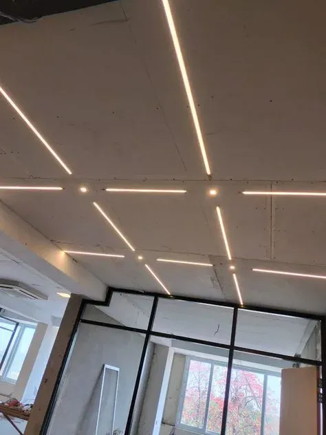 New recessed LED lights glowing in a drywall ceiling, with long linear lights and small round lights