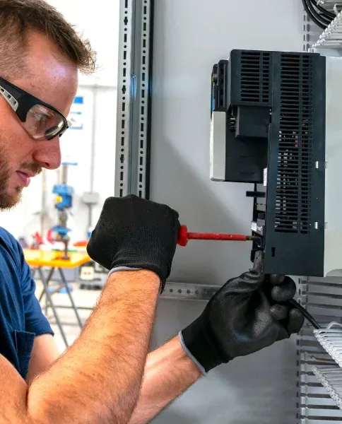 Electrician in safety glasses using a screwdriver on electrical equipment