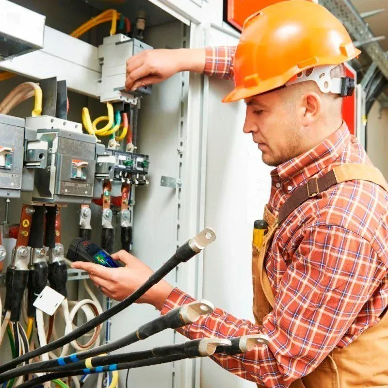 Electrician in an orange hard hat testing a commercial electrical panel with a meter