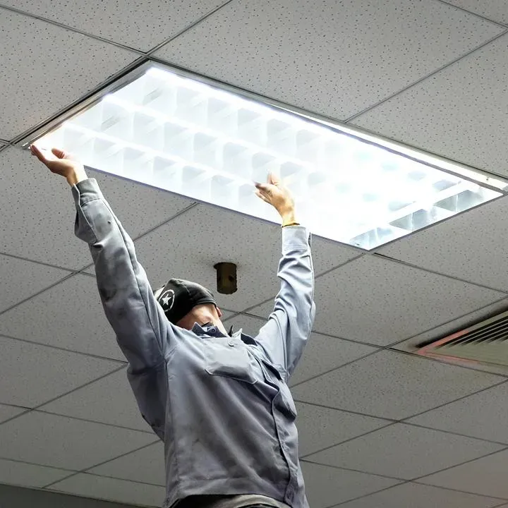 Electrician fitting an LED troffer light into a drop ceiling in an office