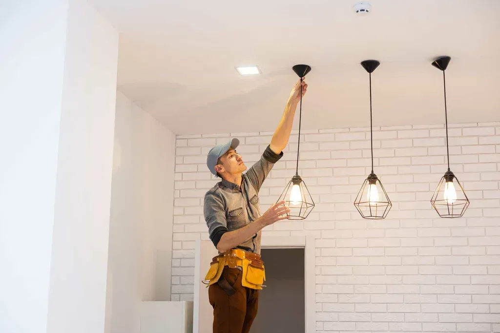 Electrician hanging a row of pendant lights with LED bulbs from a ceiling