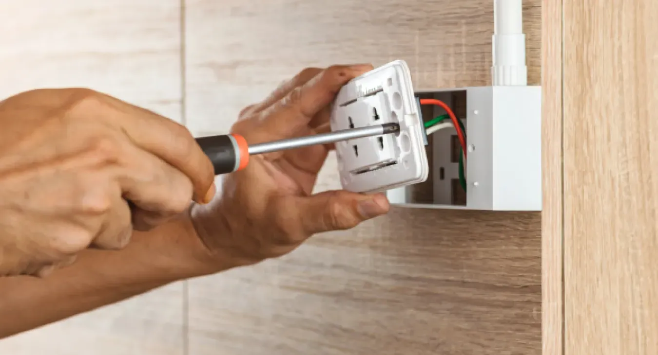 Electrician using a screwdriver to fasten an outlet into a surface mounted box