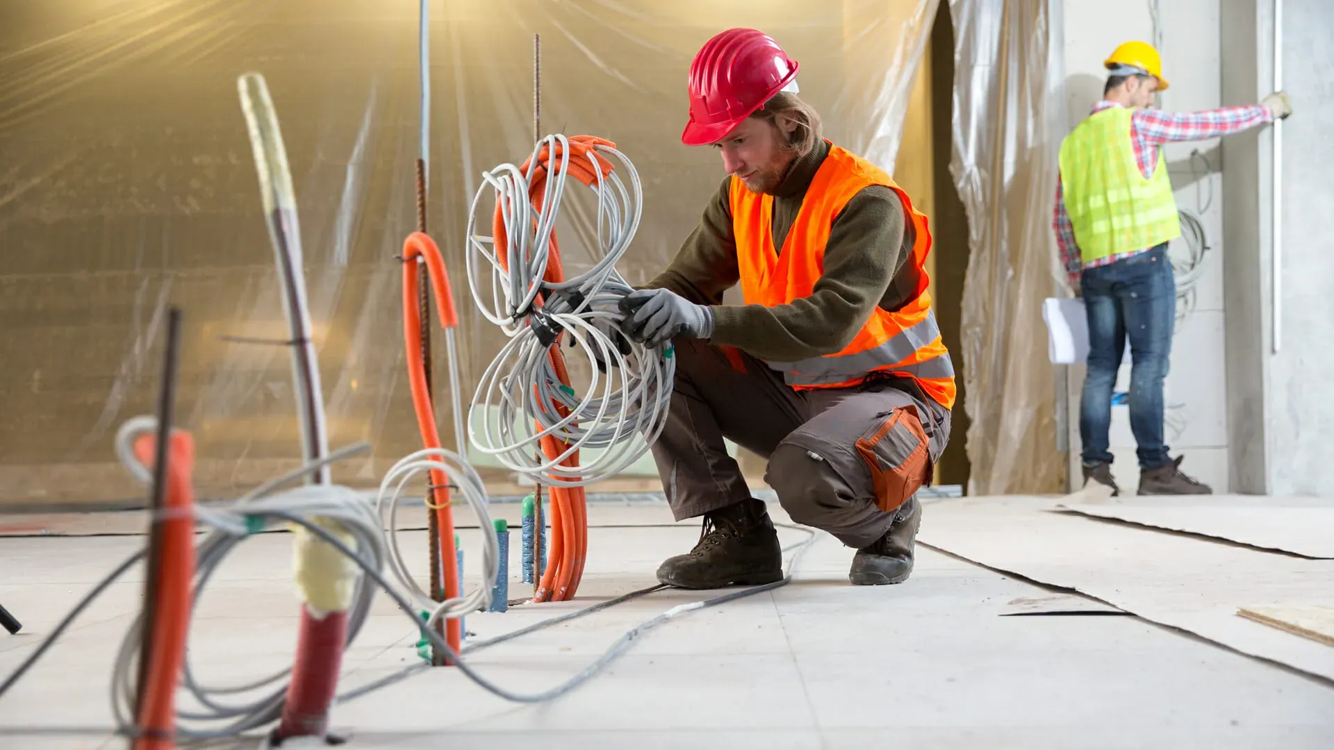 Electrician in a hard hat sorting new wiring on the floor of a commercial space under construction