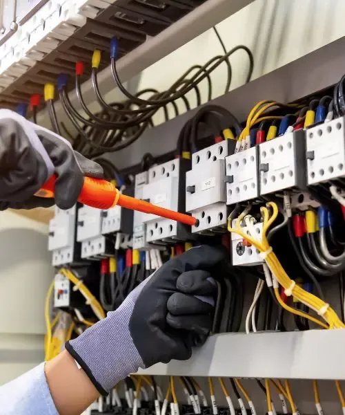 Gloved hands tightening wire connections on terminals inside a commercial electrical panel