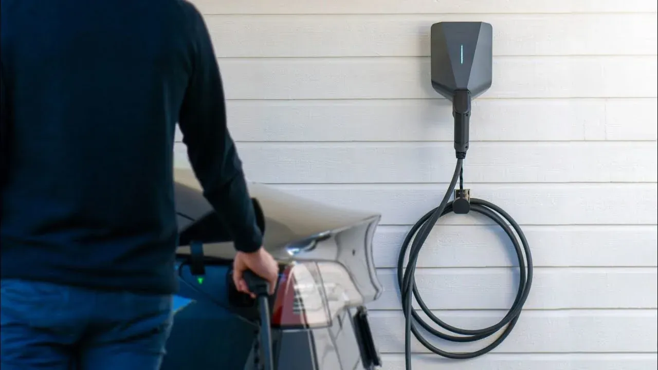 Homeowner plugging in an electric car next to a Level 2 charger on a white siding wall