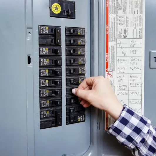 Hand switching a breaker in a home electrical panel with labeled circuits