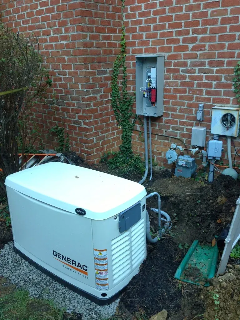 Generac 14kW standby generator beside a brick home with the transfer switch mounted on the wall above