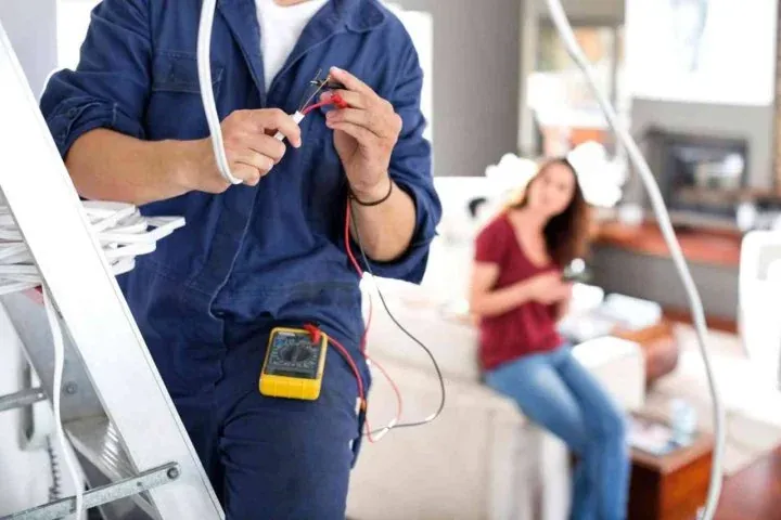 Electrician preparing a wire in a living room while the homeowner waits nearby