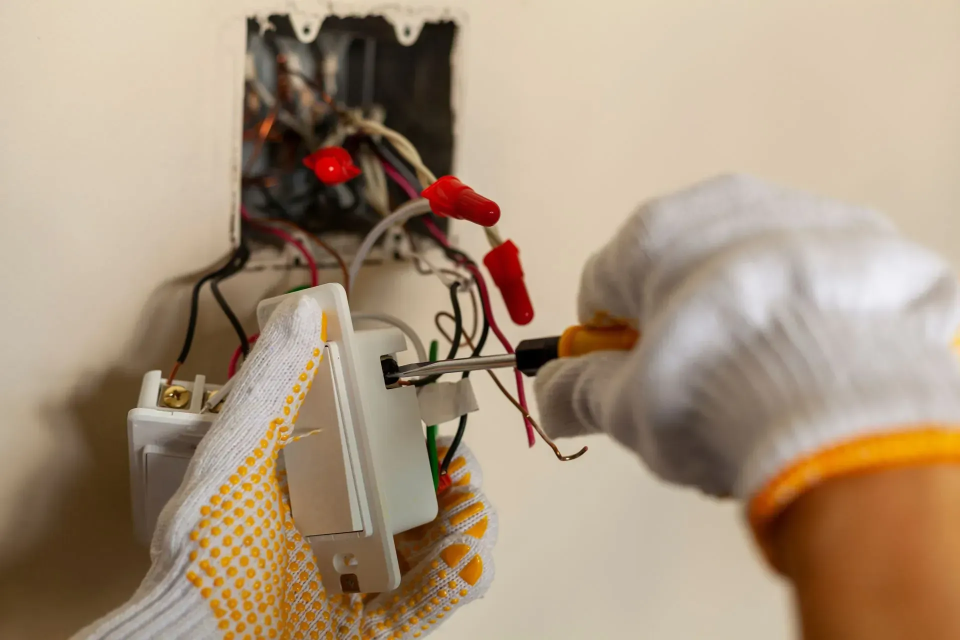 Electrician in work gloves wiring a new light switch into a wall box with a screwdriver