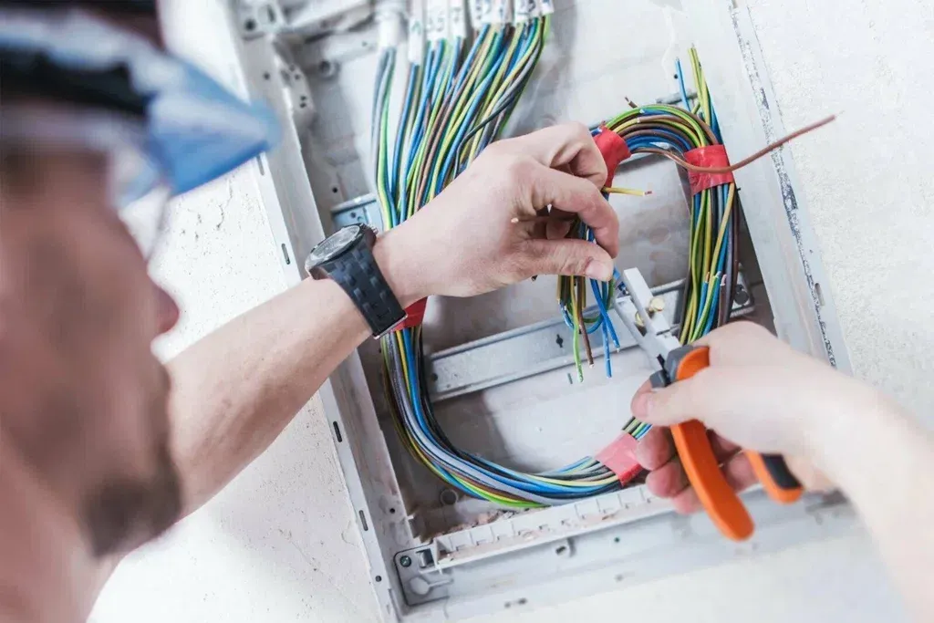 Electrician stripping wires with pliers inside a new wall mounted electrical panel