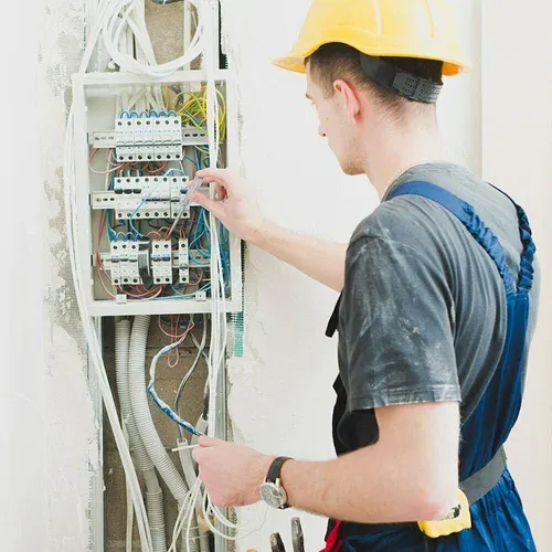 Electrician in a hard hat working on an open breaker panel in an older home