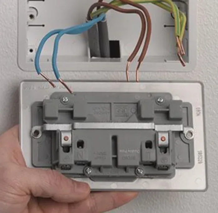 Hand holding a new outlet with its wires connected, ready to mount in the wall box