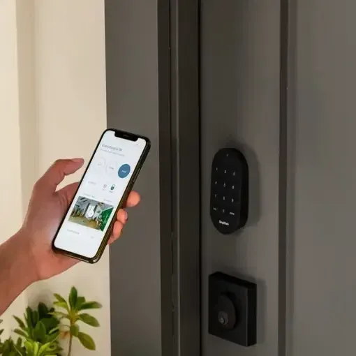Hand holding a phone with a smart home app next to a smart keypad on a front door