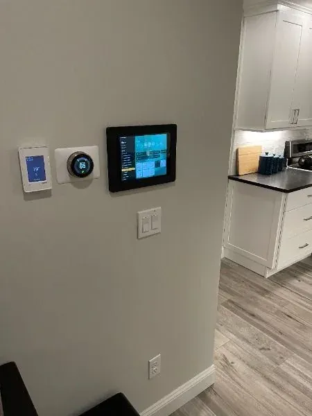 Smart thermostat, touch screen control panel and smart switches mounted on a wall near a kitchen