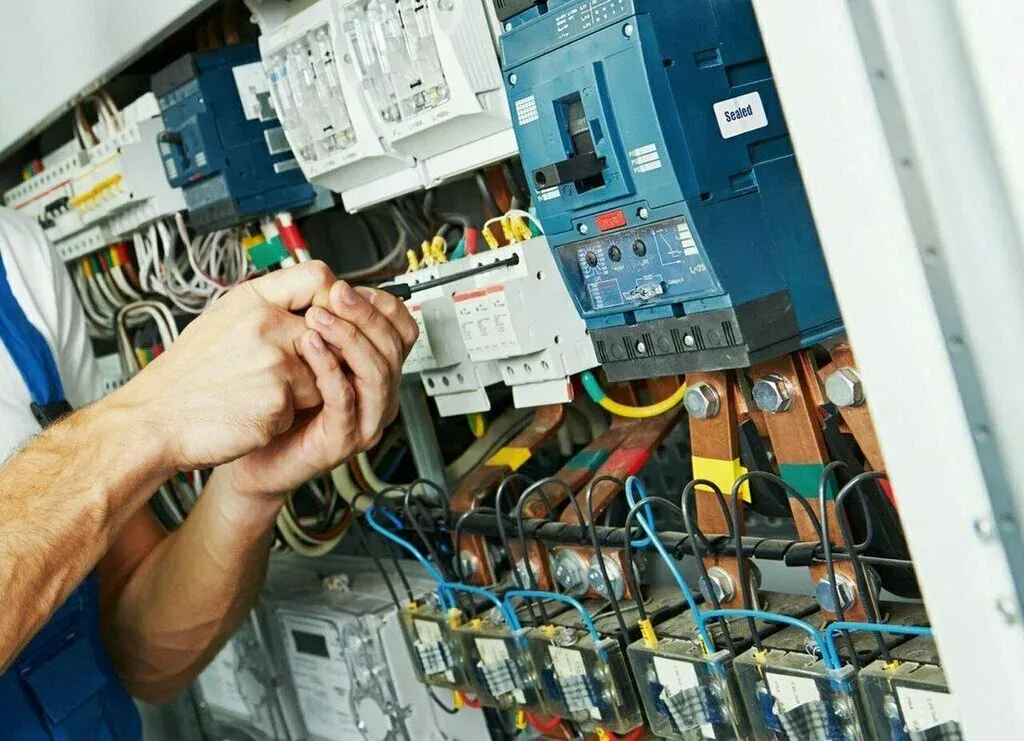 Electrician tightening a connection with a screwdriver inside an open electrical panel