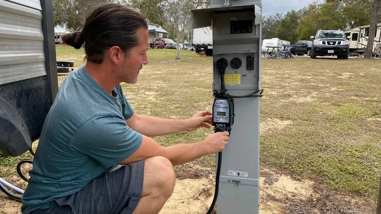 Man connecting a surge protector with a digital display to an outdoor power pedestal