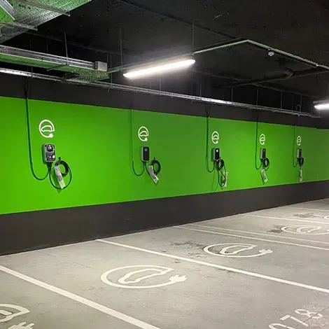 Row of wall mounted EV chargers above marked charging spaces in a parking garage